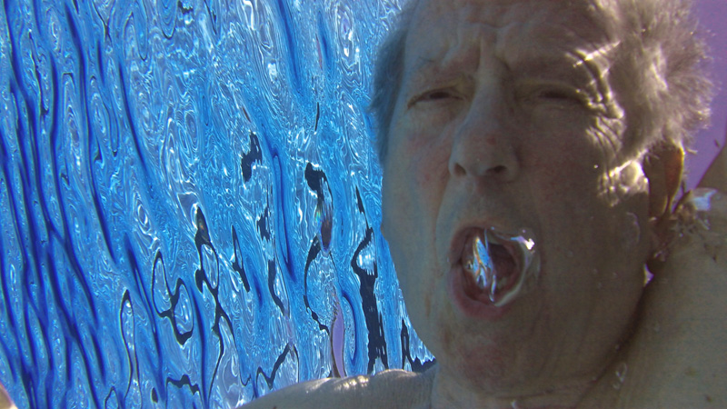 Adam with his mouth open, a bubble forming in it, submerged